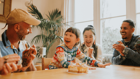 Teaching bilingual children represented by a small child sitting at a table surrounded by diverse family members.