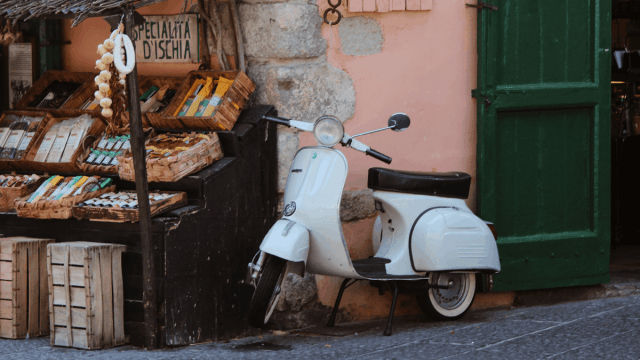 white vespa leaning against a pink wall in italy italian verbs