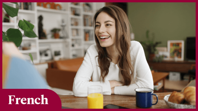A woman sitting in her living room and smiling, possibly while learning French basics