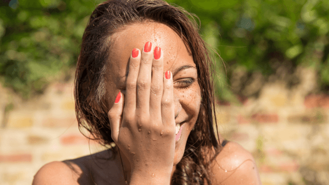 Embarrassing language mistakes represented by a woman standing in front of a brick wall, slightly covering her face with her hand and laughing.