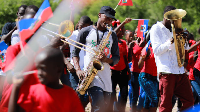 Haitian heritage month represented by a Haitian parade with saxophone, trombone and euphonium players decked out in the Haitian flag