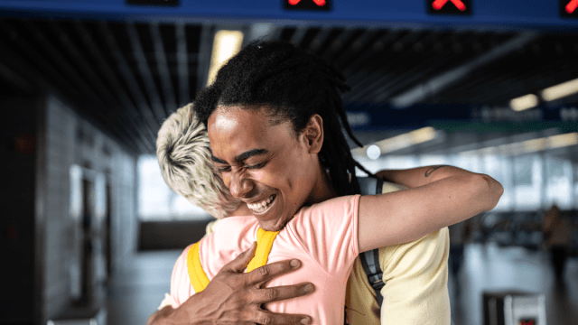 How to say hello in Portuguese represented by two friends embracing each other at an airport