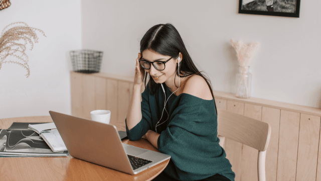 A woman sitting at her laptop using headphones to listen to Turkish podcasts