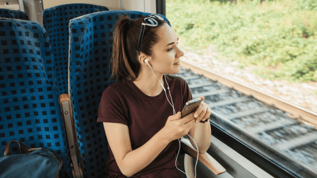 A woman sitting on a train, listening to Polish podcasts on her phone