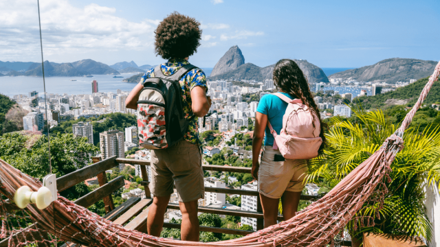 pair of tourists wearing backpacks gazing at skyline and mountains of ipanema common portuguese verbs