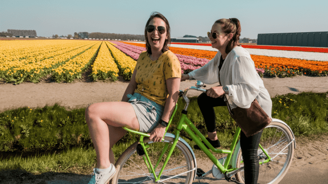 Tips for learning Dutch represented by two girls riding a bicycle through a field of tulips.
